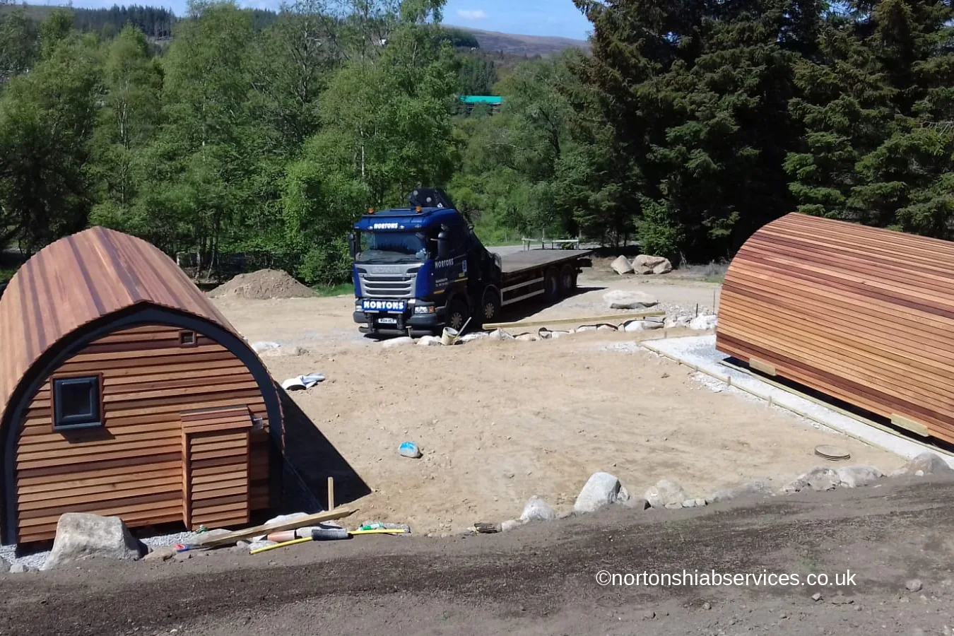 Two cedar glamping pods set down on prepared bases with a Nortons hiab alongside