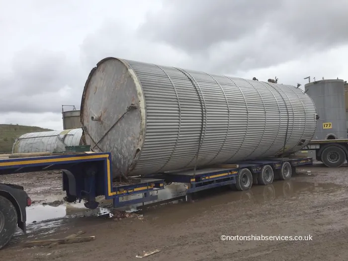 A steel silo secured on a Nortons trailer bed with a tank yard behind