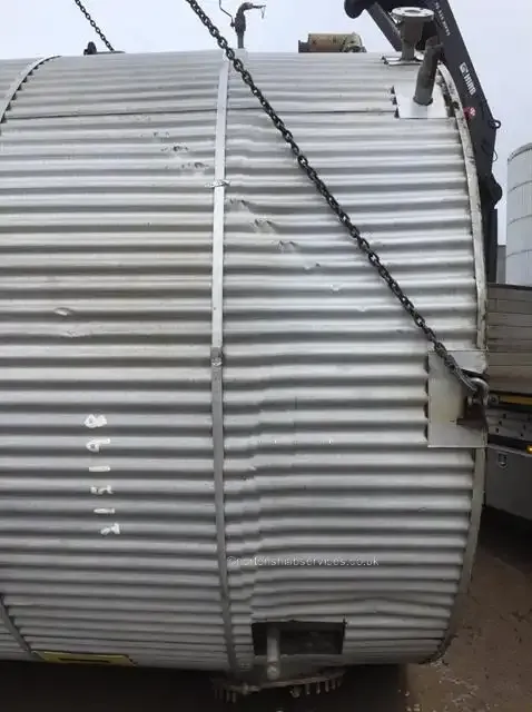 A corrugated steel silo section held in lifting chains by a Nortons crane