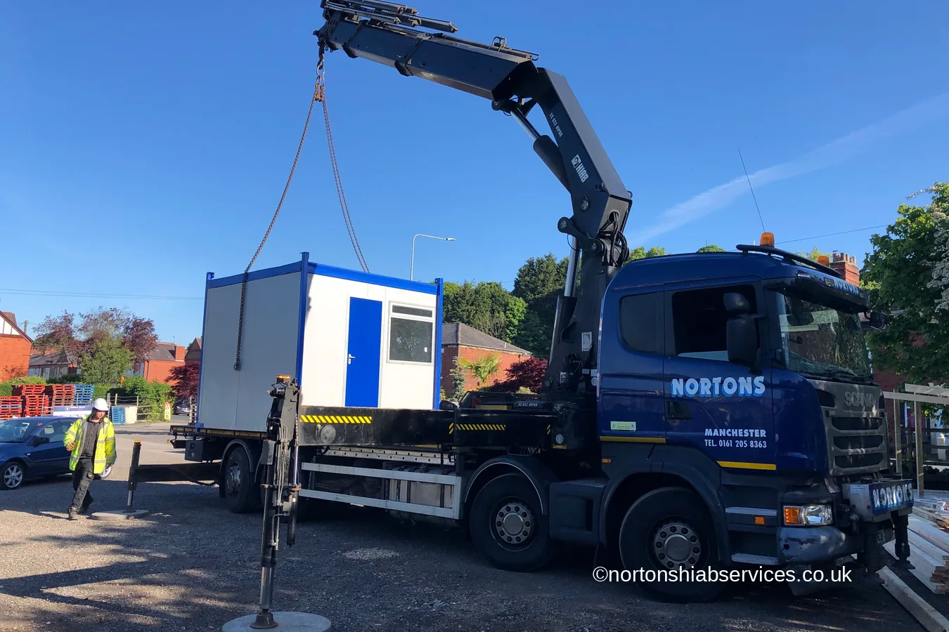 A refurbished blue and white office cabin suspended from a Nortons hiab