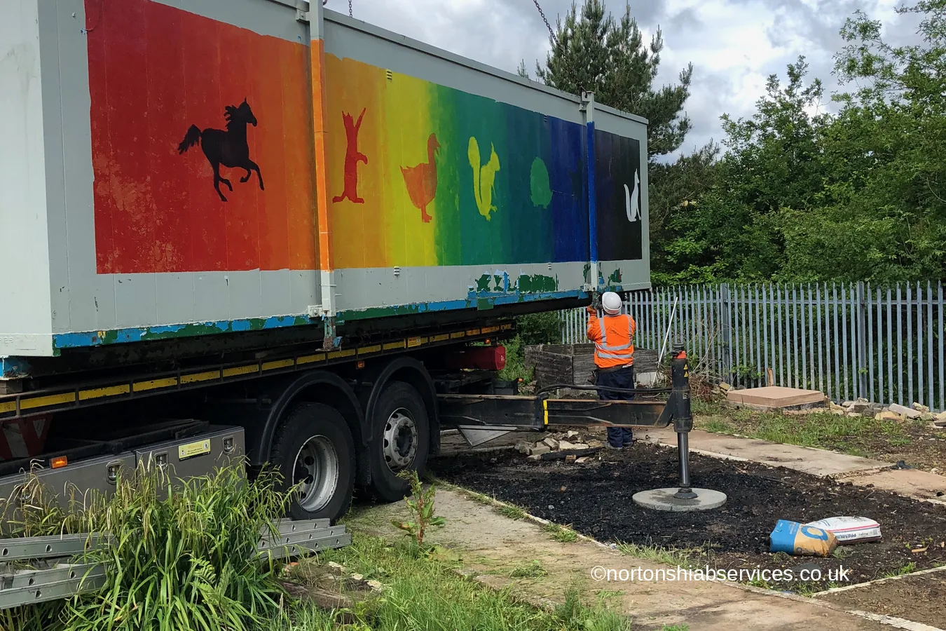 A brightly painted community cabin being lifted by a Nortons hiab at Carrbrook