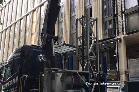 Sections of a builders hoist loaded onto a Nortons lorry beside a tower block in Manchester