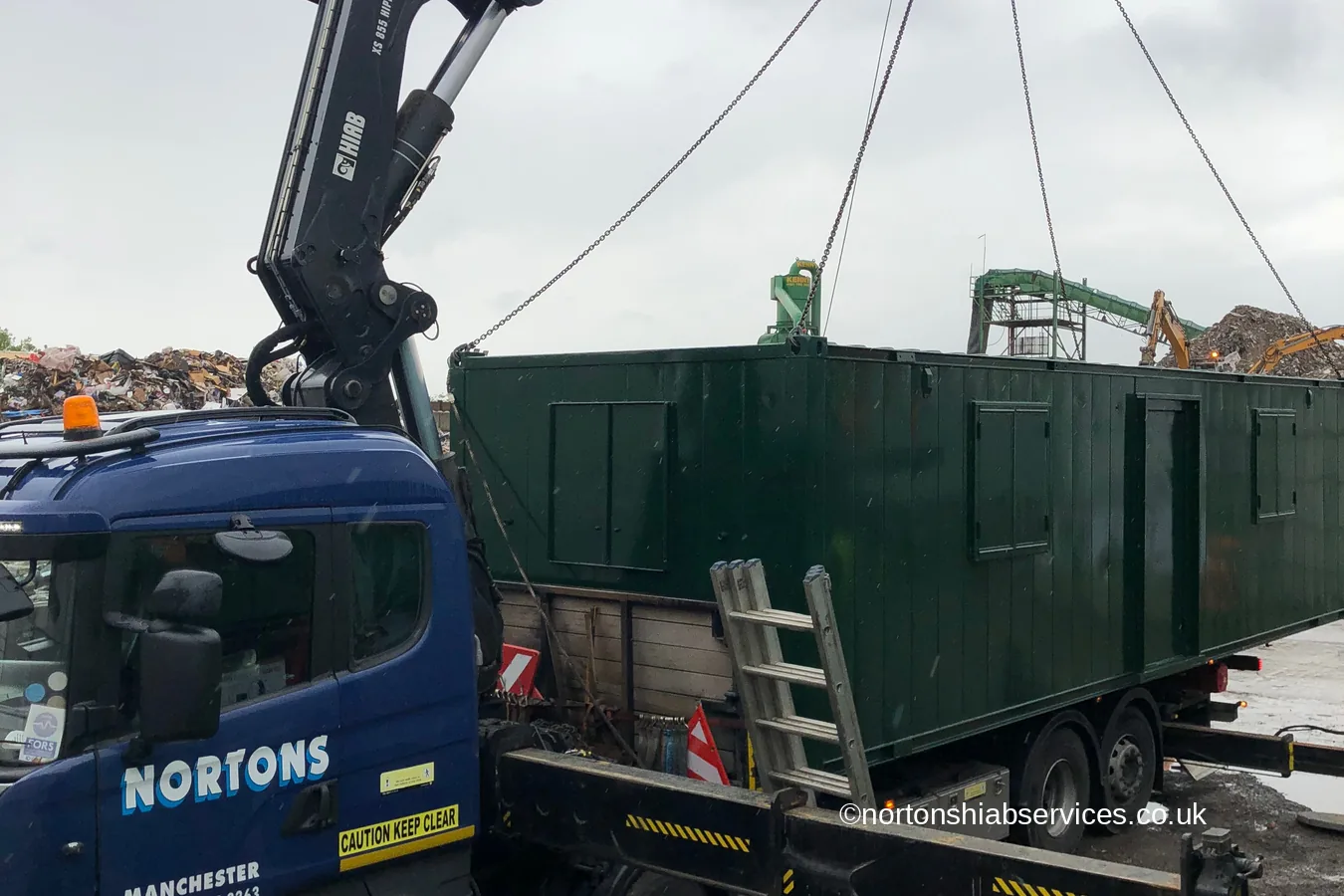 A large anti-vandal cabin being lifted over a stack of existing units