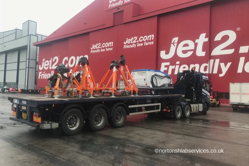 Orange aircraft jacking trestles and ground power units loaded on a Nortons trailer at an airport