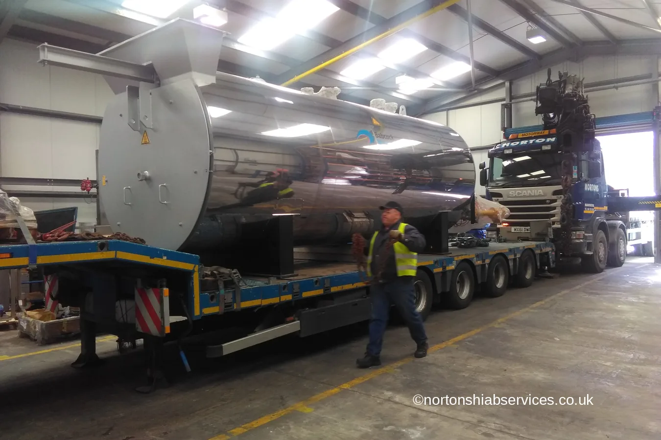 A large machine being unloaded from a Nortons low loader inside a works building