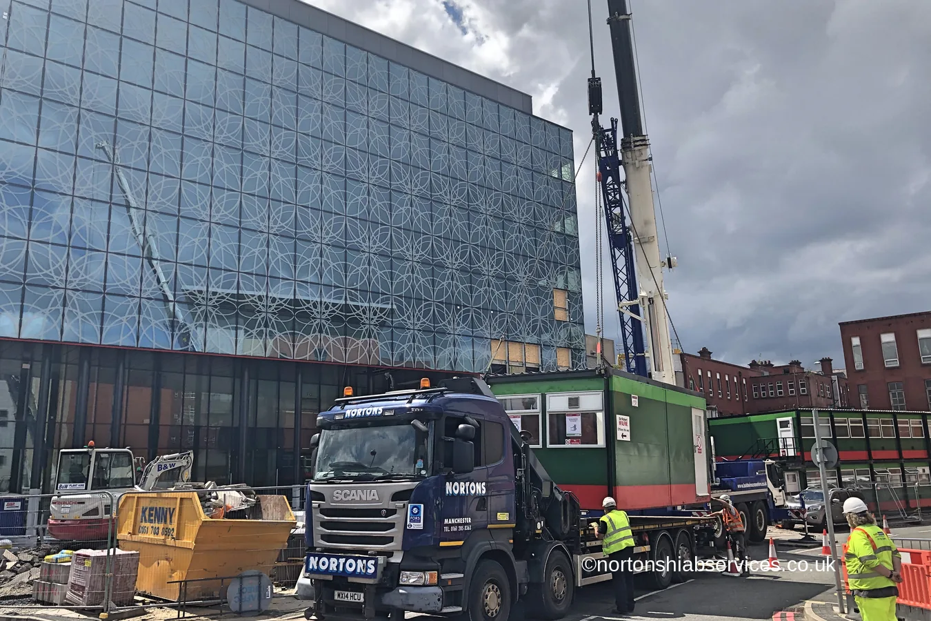 A site cabin loaded onto a Nortons hiab outside a completed city centre building