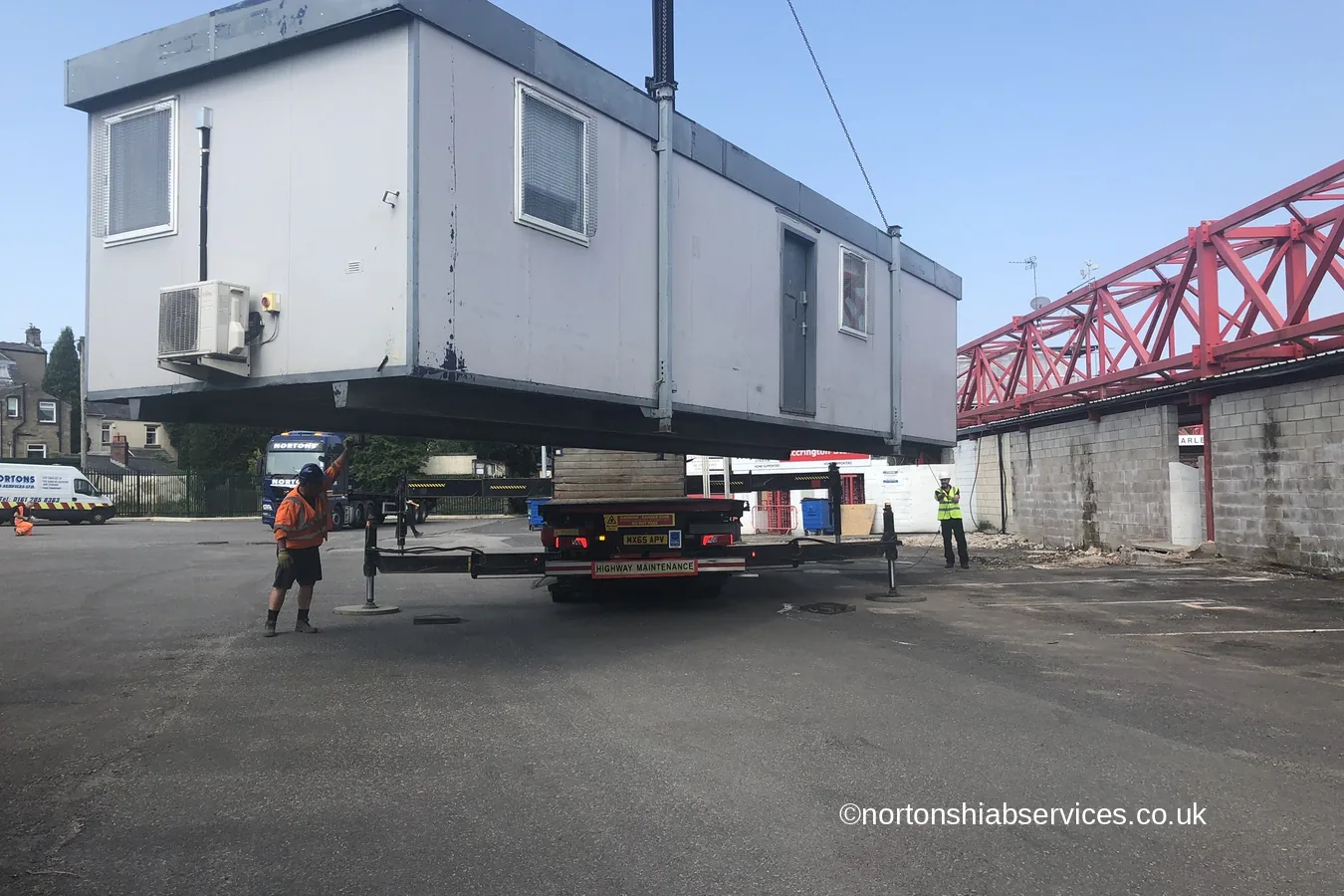 A portable cabin on a Nortons hiab lorry beside a football stand