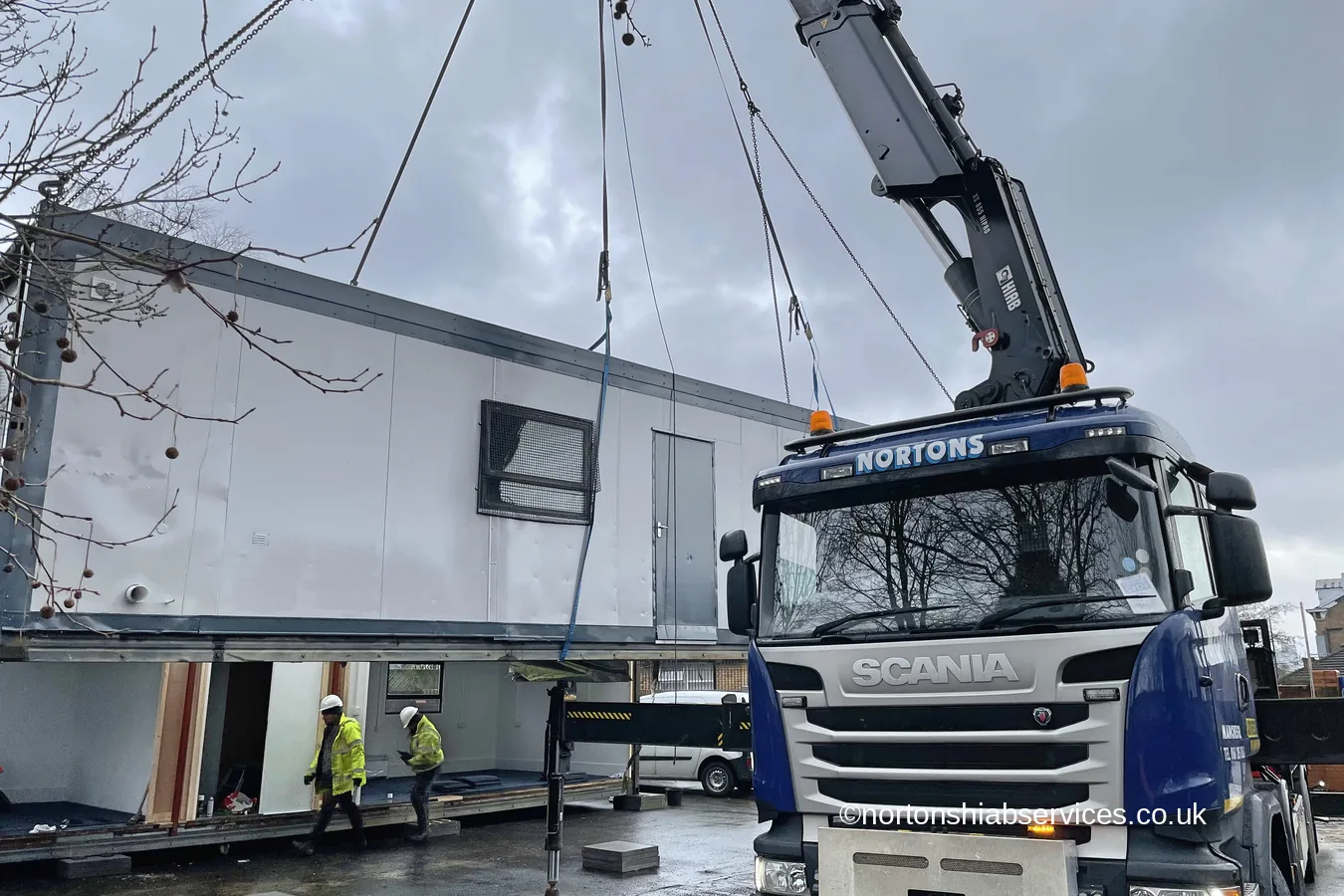 A Nortons crane landing a modular classroom onto its base with the crew steadying it
