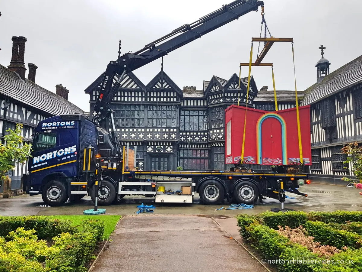 A red travelling arts centre structure loaded on a Nortons trailer outside a timbered hall