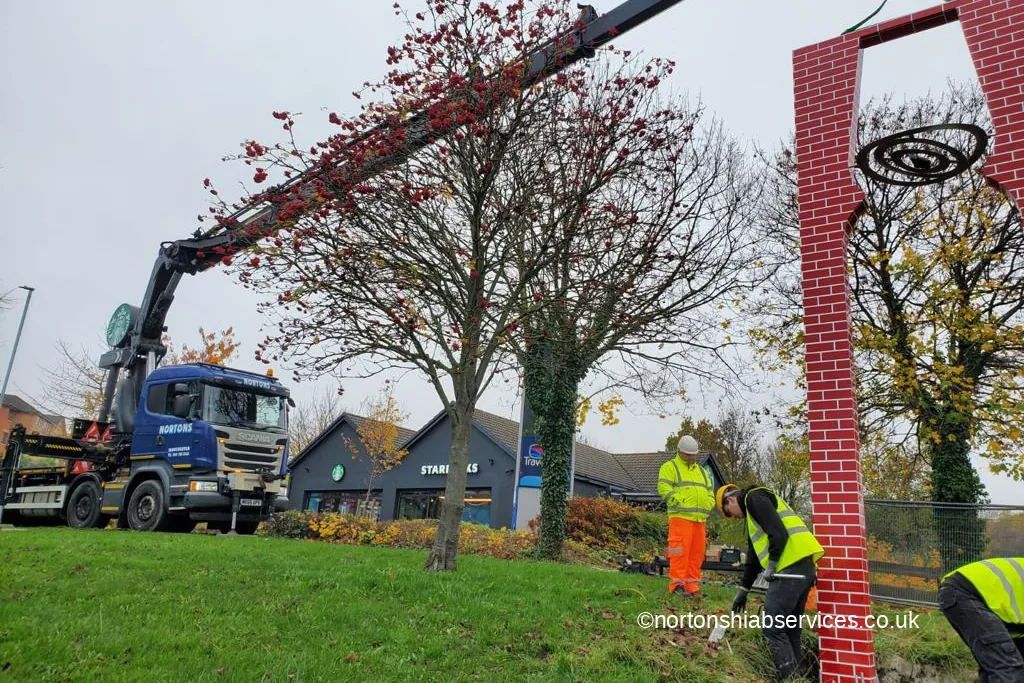 A tall gateway sign held plumb on a Nortons crane strop while the crew fix the base