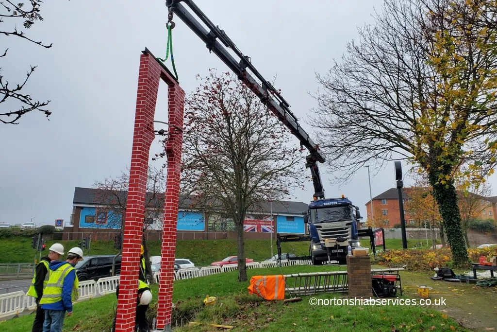 A Nortons crane holding a tall brick clad gateway sign upright at Barnsley