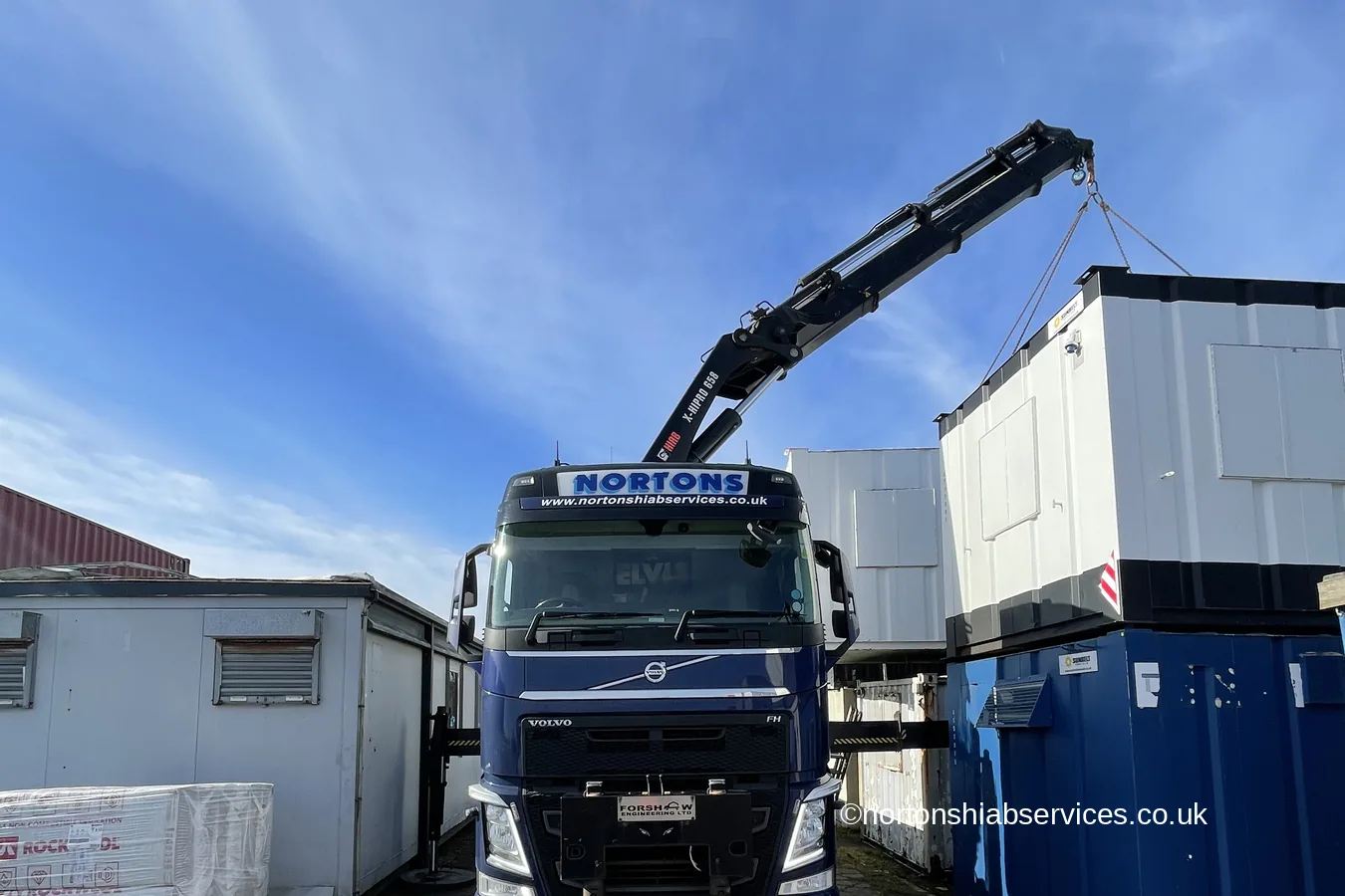 A Nortons 658 wagon and drag lifting portable cabins in a yard