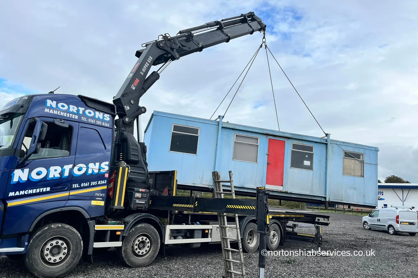 A portable cabin being lowered onto hardstanding by a Nortons hiab