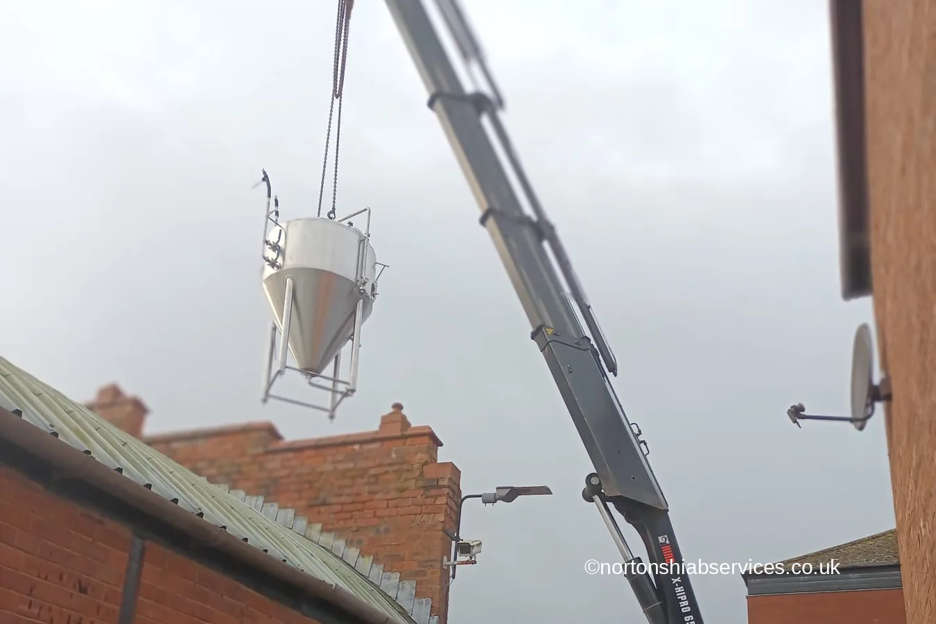 A Nortons rigid 658 hiab lifting a brewing tank over a brick wall