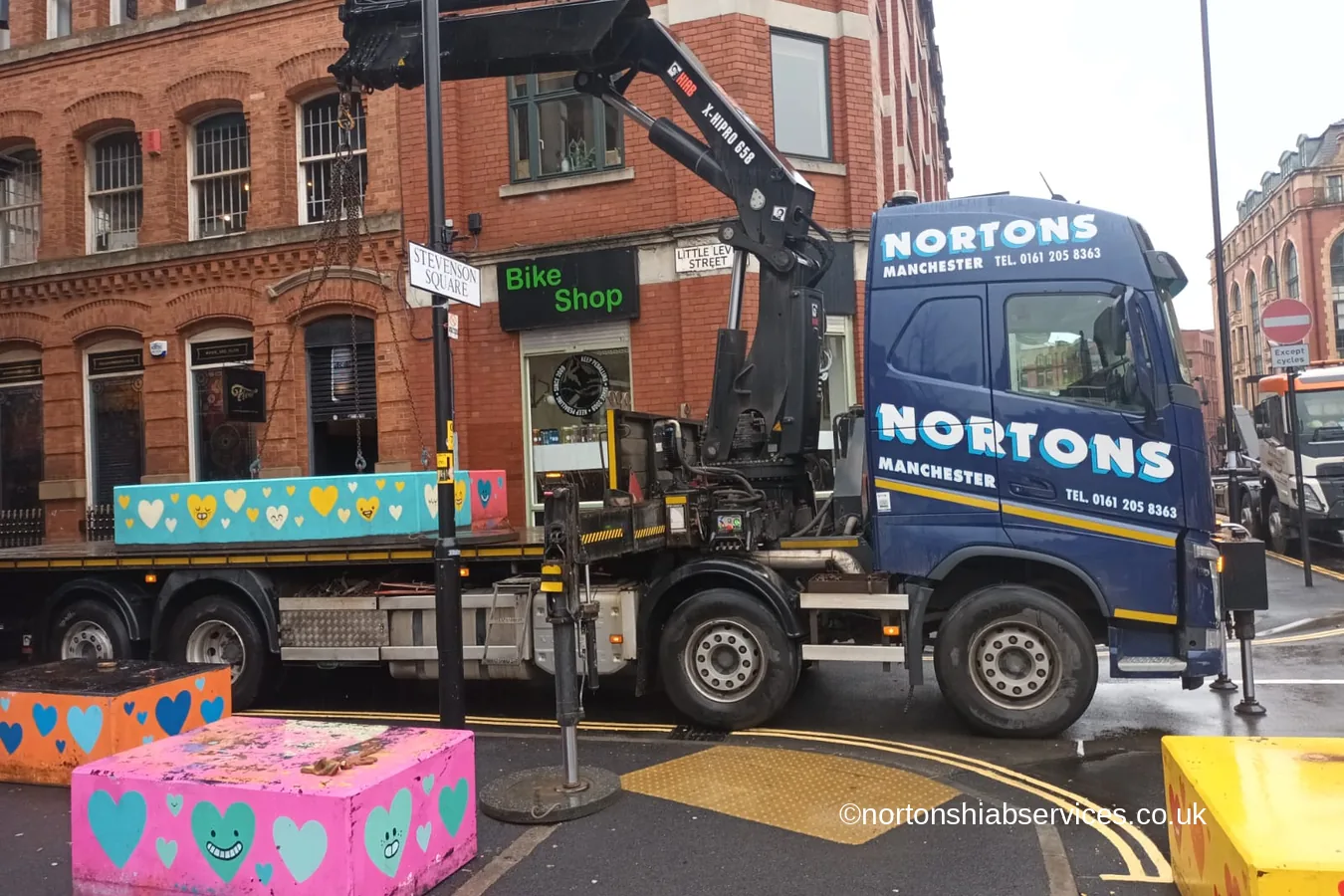 A brightly painted concrete bollard being set down in a Manchester city centre street