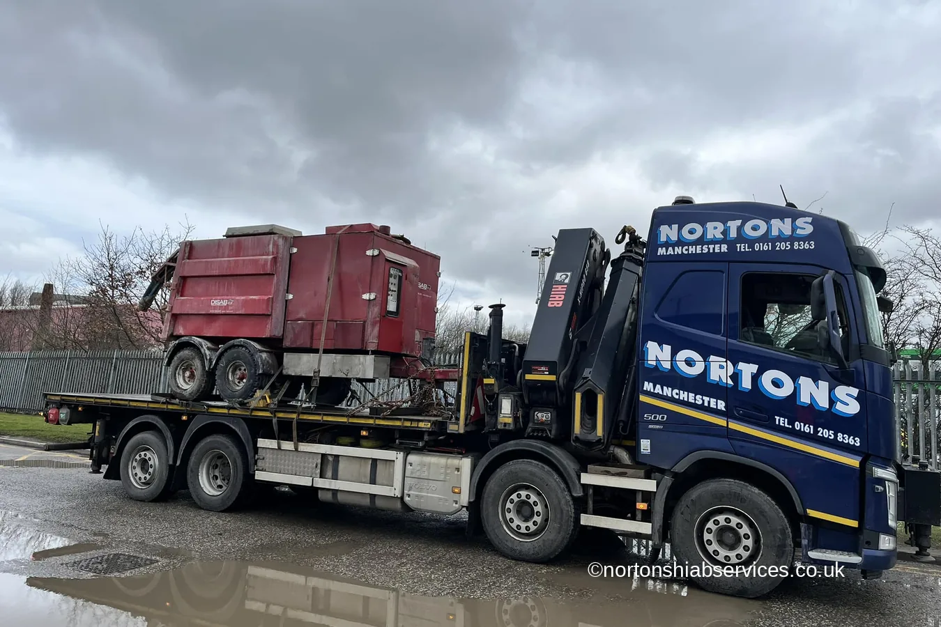 A waste compactor loaded on the bed of a Nortons hiab lorry