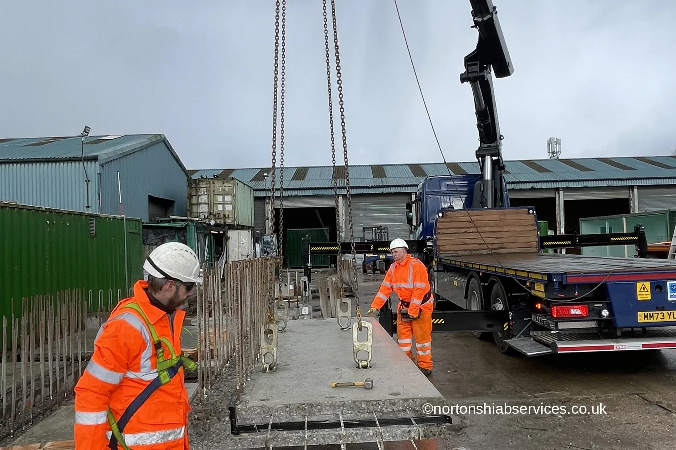 Site operatives guiding a precast concrete plank into position over reinforcement