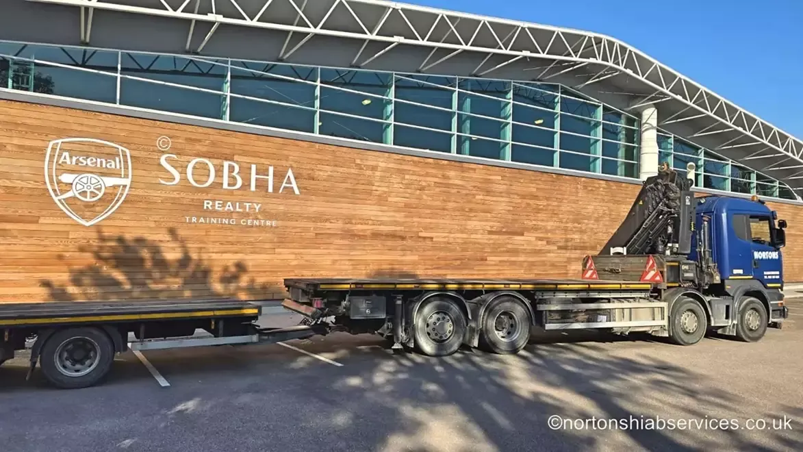 A Nortons artic and trailer loaded outside the timber-clad frontage of Arsenal's training ground