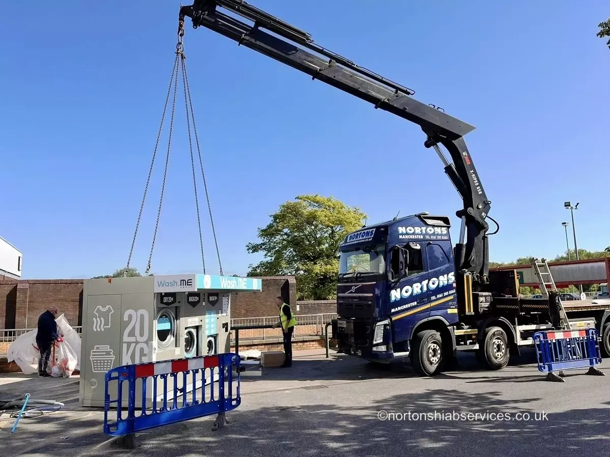 Nortons hiab lifting a packaged laundry unit off the trailer bed