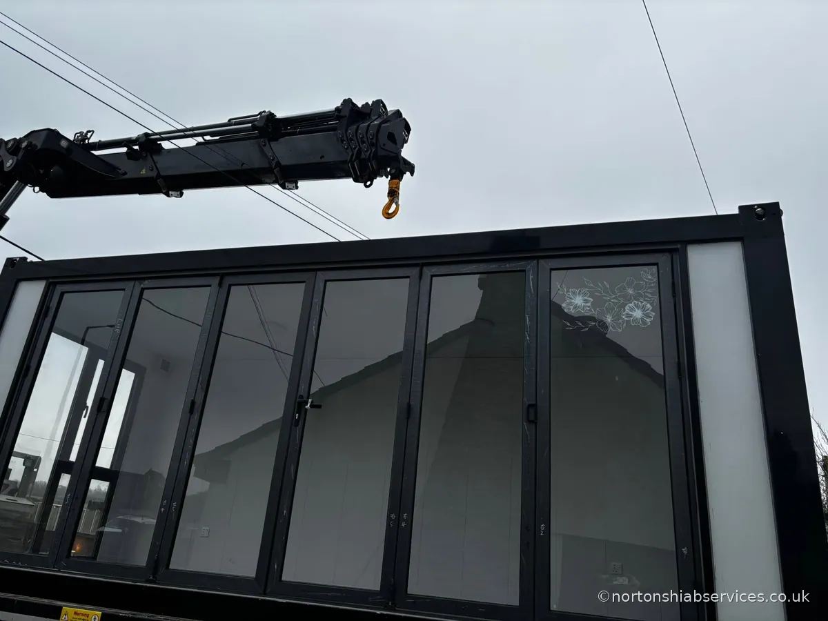 A Nortons crane holding a large glazed structure with full-height windows at Droylsden