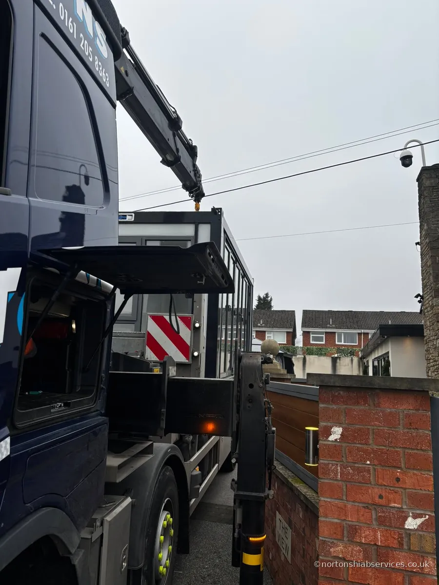 A Nortons hiab with the boom raised from the street to reach over a brick boundary wall at Droylsden