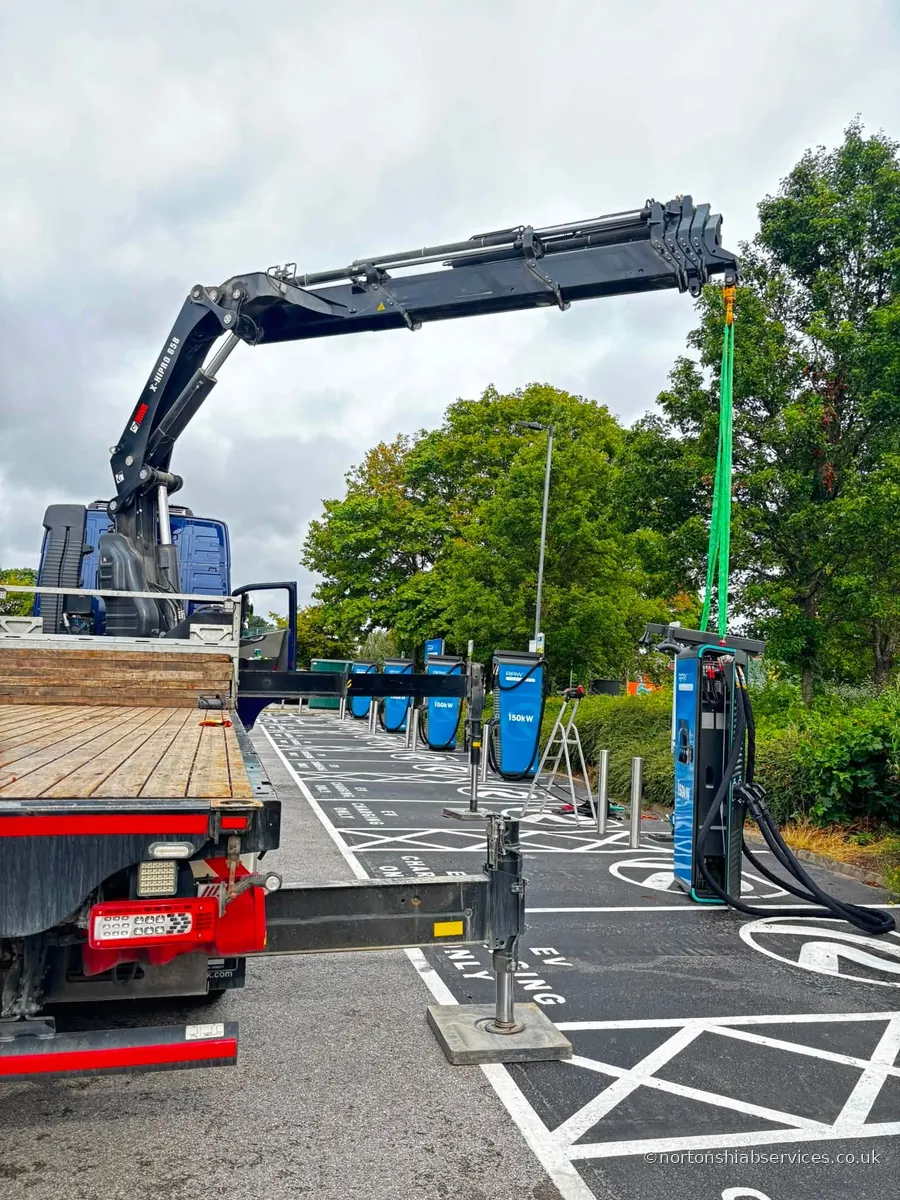 A Nortons hiab with the boom extended over a row of EV rapid charging bays with the stabiliser legs down