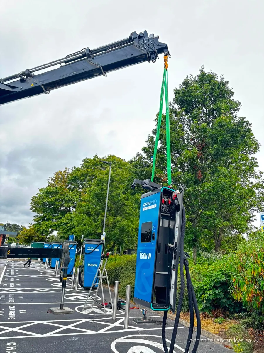 A Nortons crane lifting a blue EV rapid charging unit on slings at a charging hub