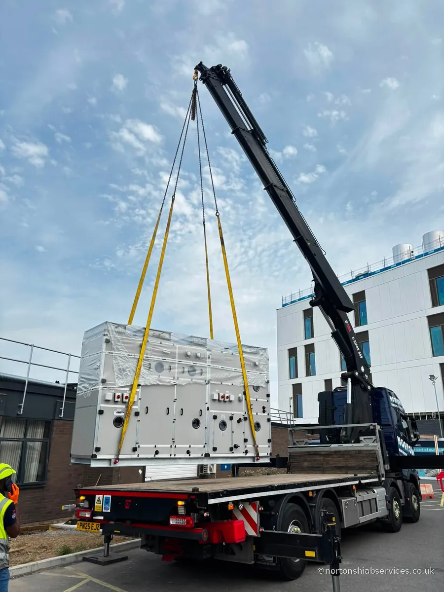 A Nortons hiab holding a large wrapped plant unit in the air on yellow slings outside Royal Shrewsbury Hospital