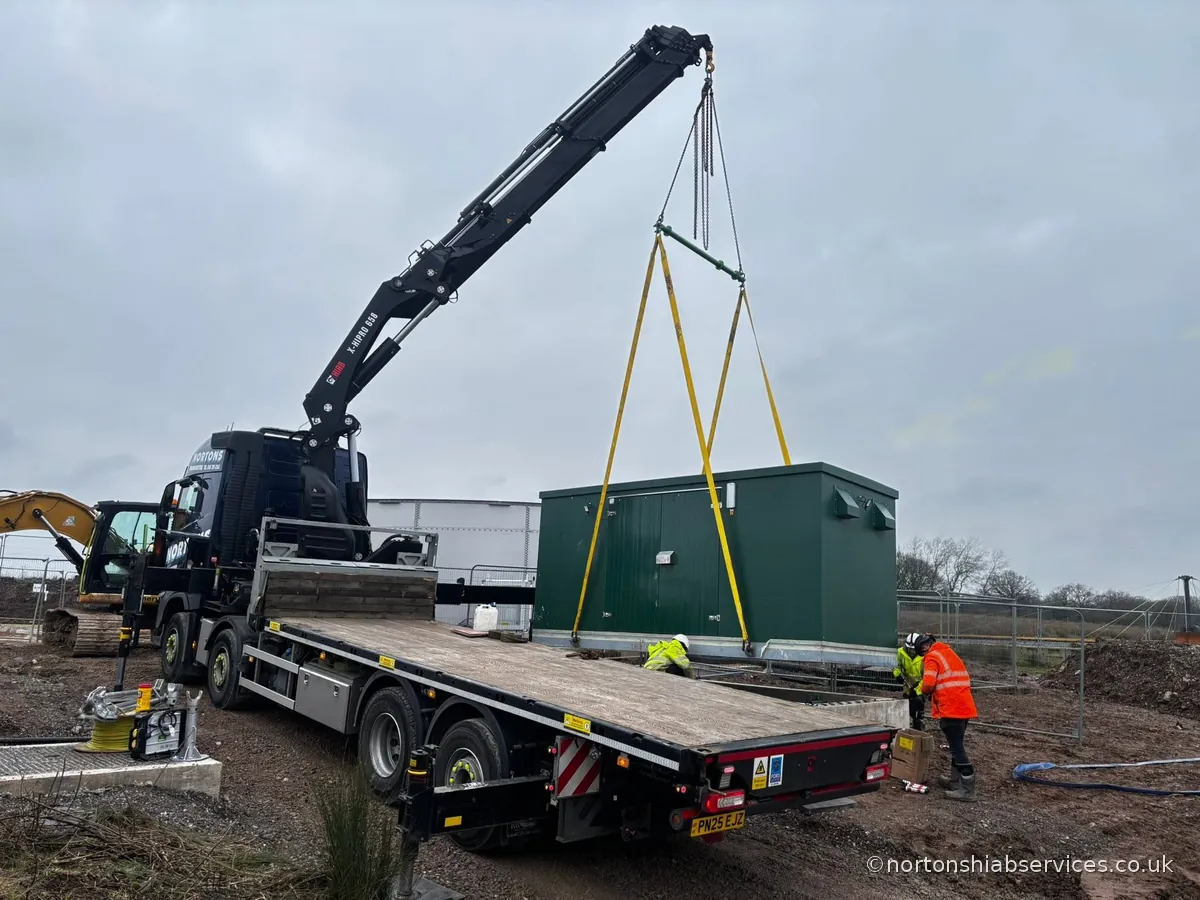 A Nortons hiab lifting a green packaged kiosk building off the lorry bed at Winsford in Cheshire