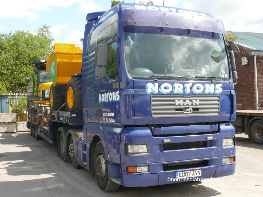 Yellow plant machine loaded on the bed of a Nortons hiab lorry