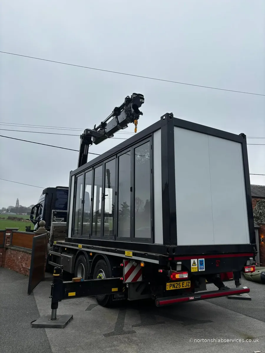 A large glazed garden room loaded on the bed of a Nortons hiab lorry in a residential street, ready to travel
