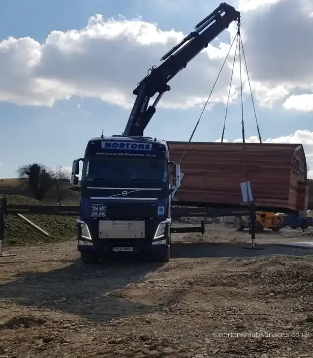 Glamping pod being craned over a fence by a Nortons hiab