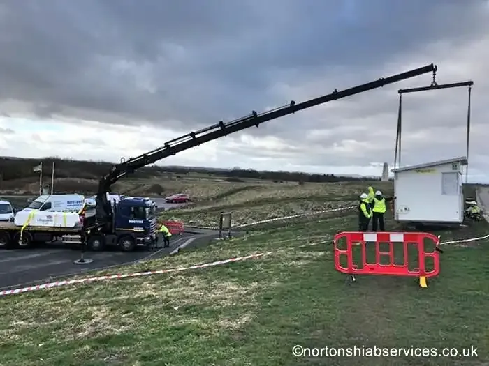 A Nortons rigid with its boom extended setting a cabin down on open moorland