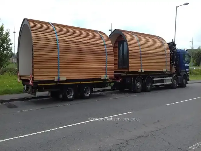 A Nortons rigid and drawbar trailer carrying two timber glamping pods on the road