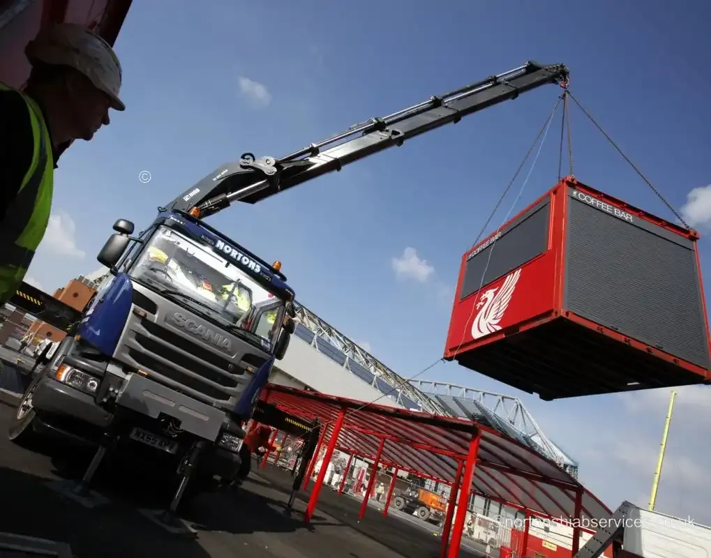 A Nortons hiab holding a red site unit on the slings above the trailer at Anfield