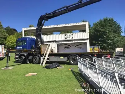 Container unit and crowd barriers on grass at a festival site with a Nortons hiab