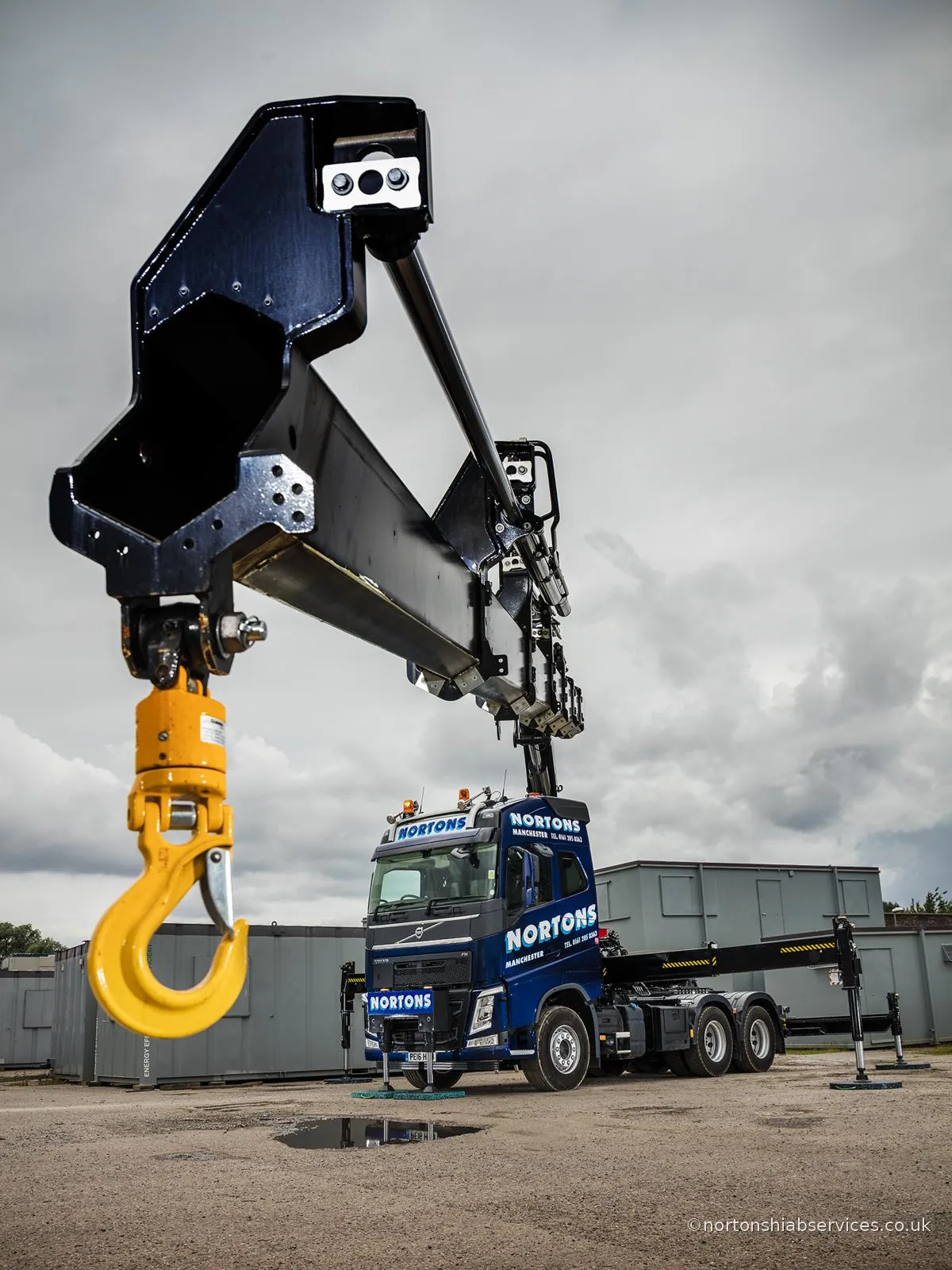 Nortons hiab standing on its stabiliser legs with the boom raised and the main hook out over the yard