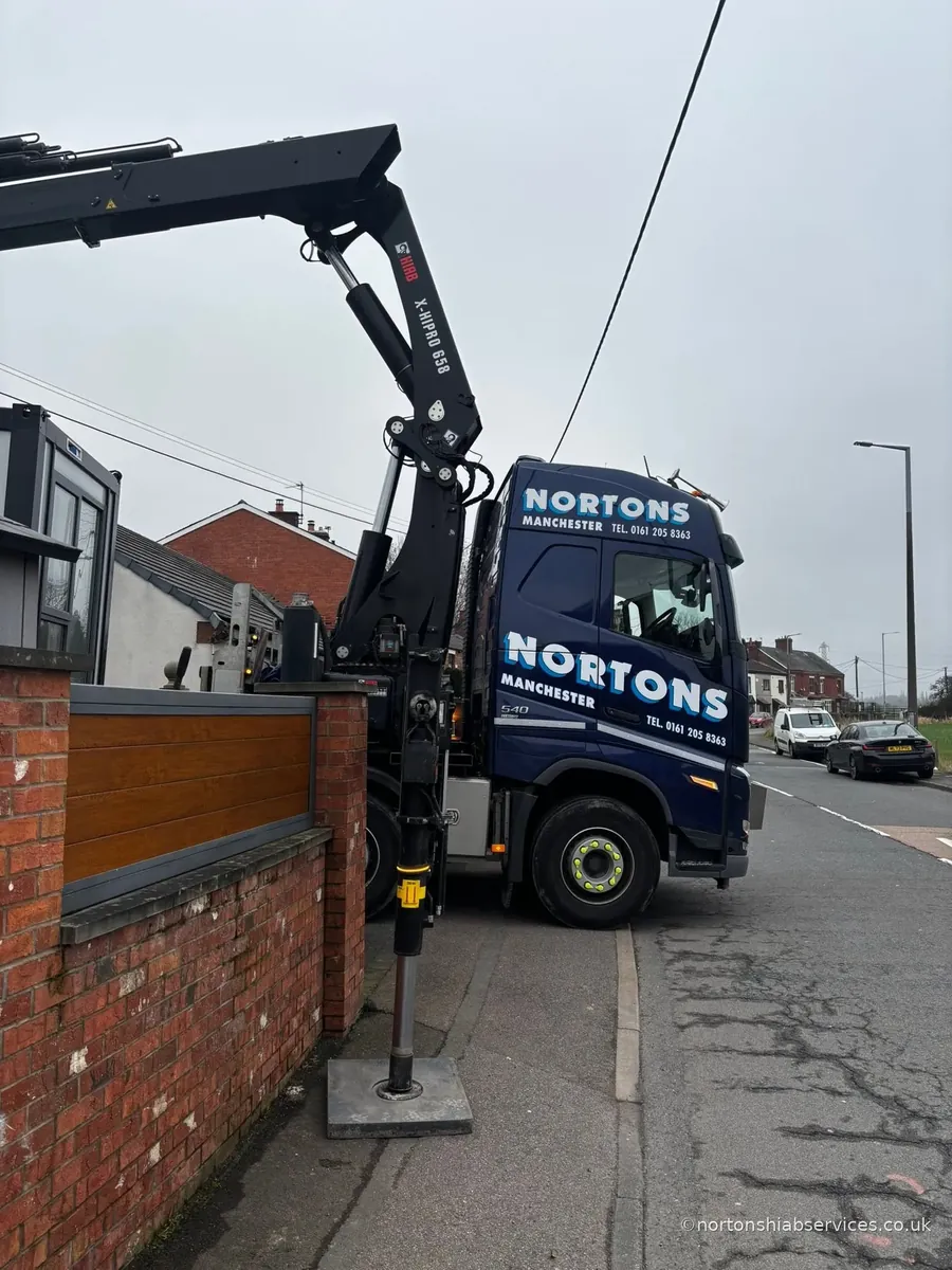 A Nortons hiab lorry set up in a narrow residential street with a stabiliser leg down on a spreader pad against a brick wall