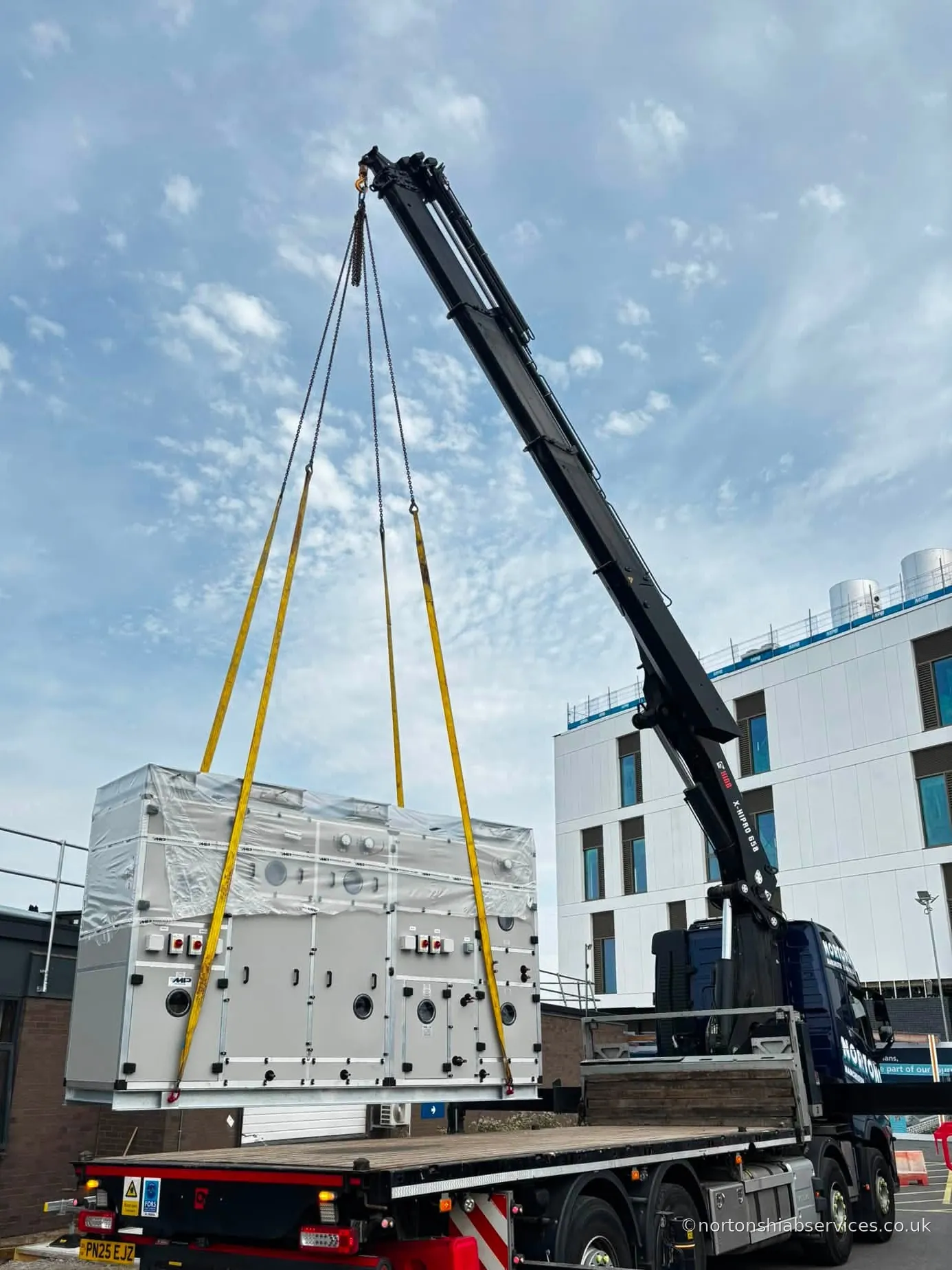 Nortons hiab lifting a large plant unit off the flatbed alongside a hospital building