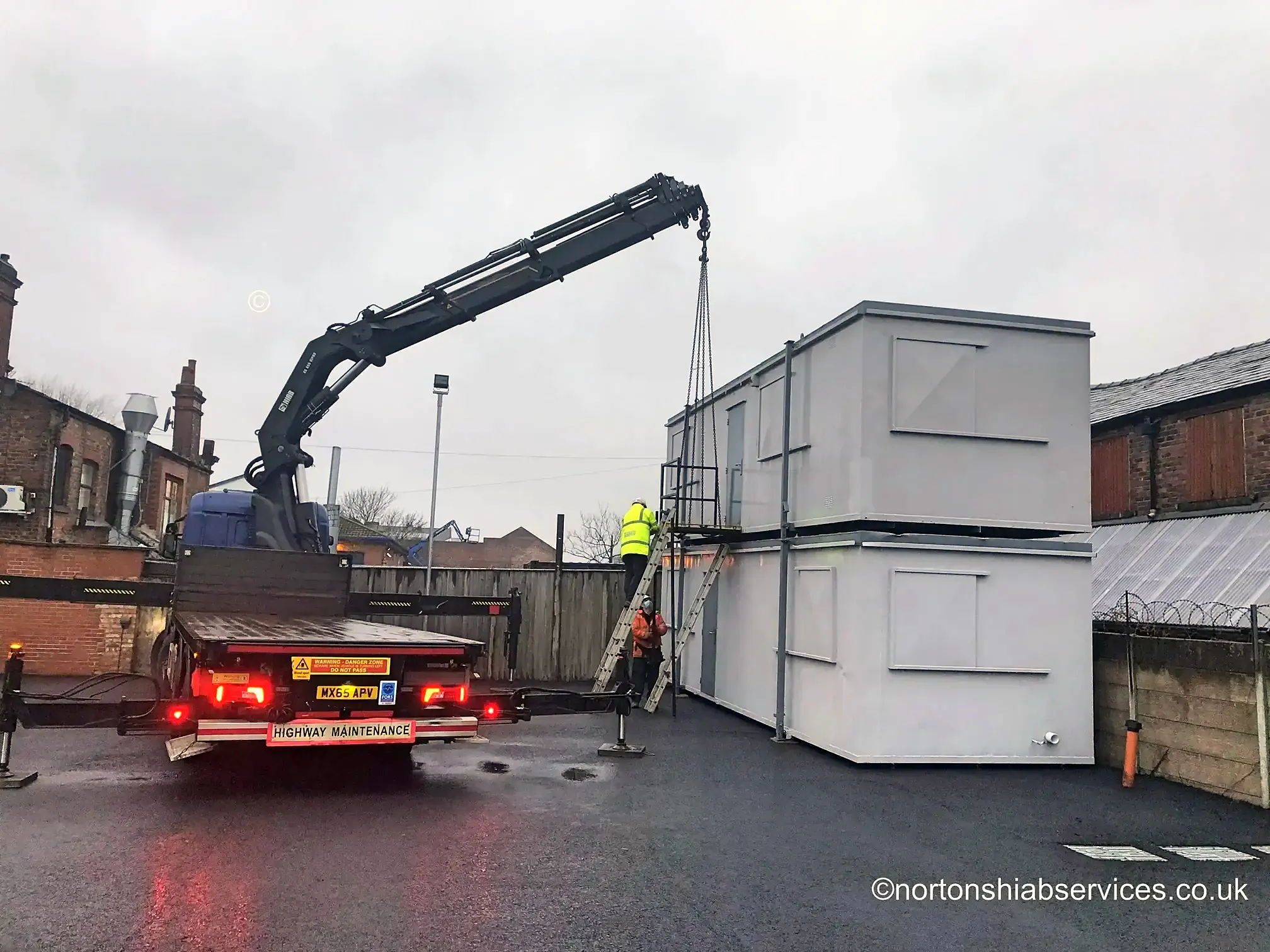 Portable cabins stacked two high on a wet evening with a Nortons lorry alongside
