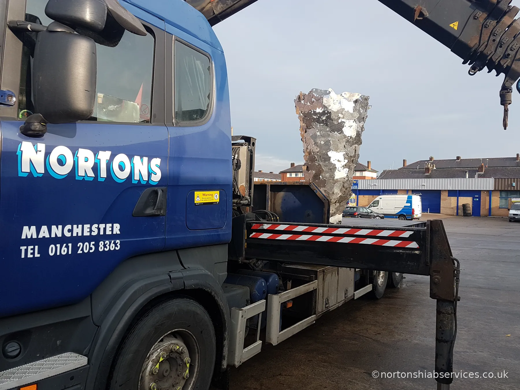 A Nortons Scania hiab with a tall metal sculpture held on the crane hook behind the cab