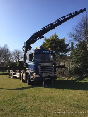 A Nortons Scania hiab standing on the grass with its crane boom extended out across the green