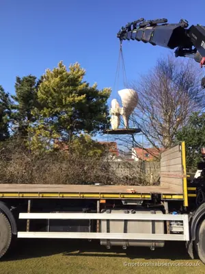 The white cast sculpture carried on the crane over a boundary wall towards its position
