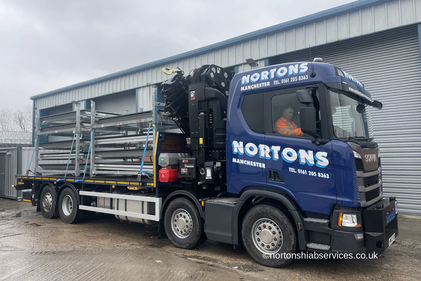 A Nortons crane lorry loaded with galvanised racking alongside a modern industrial unit