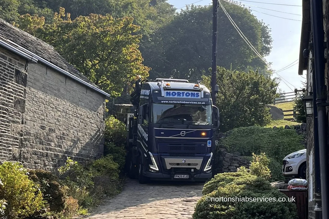 A Nortons crane lorry working its way up a narrow cobbled lane between stone walls