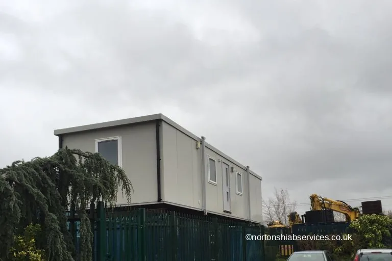 A long site office delivered by Nortons standing behind a green palisade fence on an industrial estate in Bolton