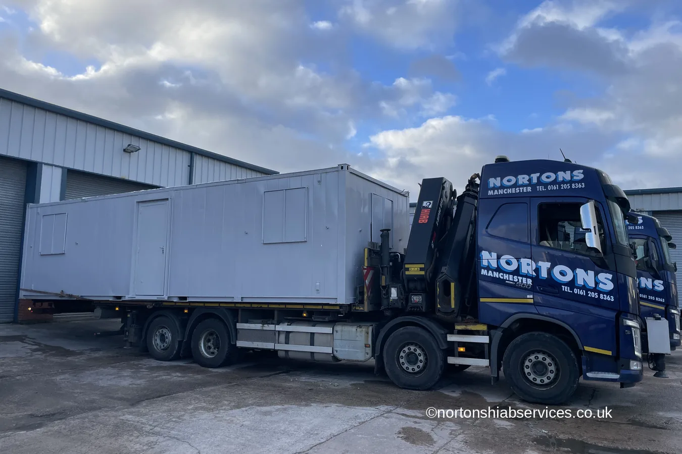 A long refurbished cabin loaded on a Nortons crane lorry outside a distribution unit