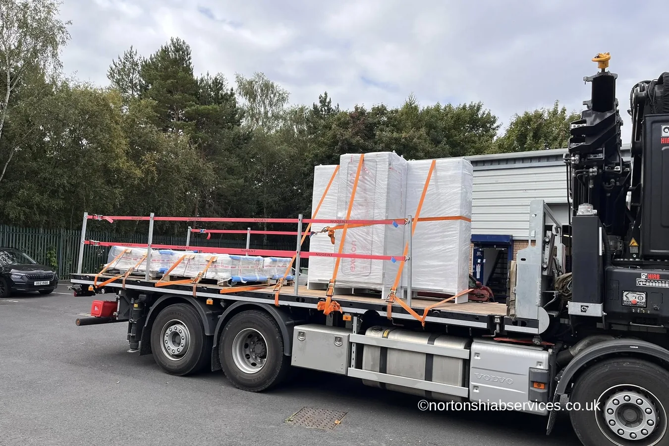 Shrink-wrapped panels strapped down under orange webbing on the bed of a Nortons crane lorry