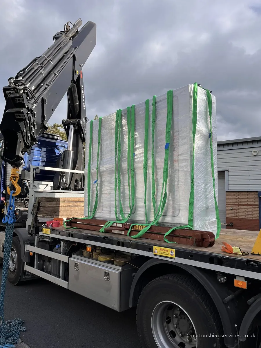 A Nortons hiab lorry loaded with shrink-wrapped panels held in green slings on the bed at an industrial unit