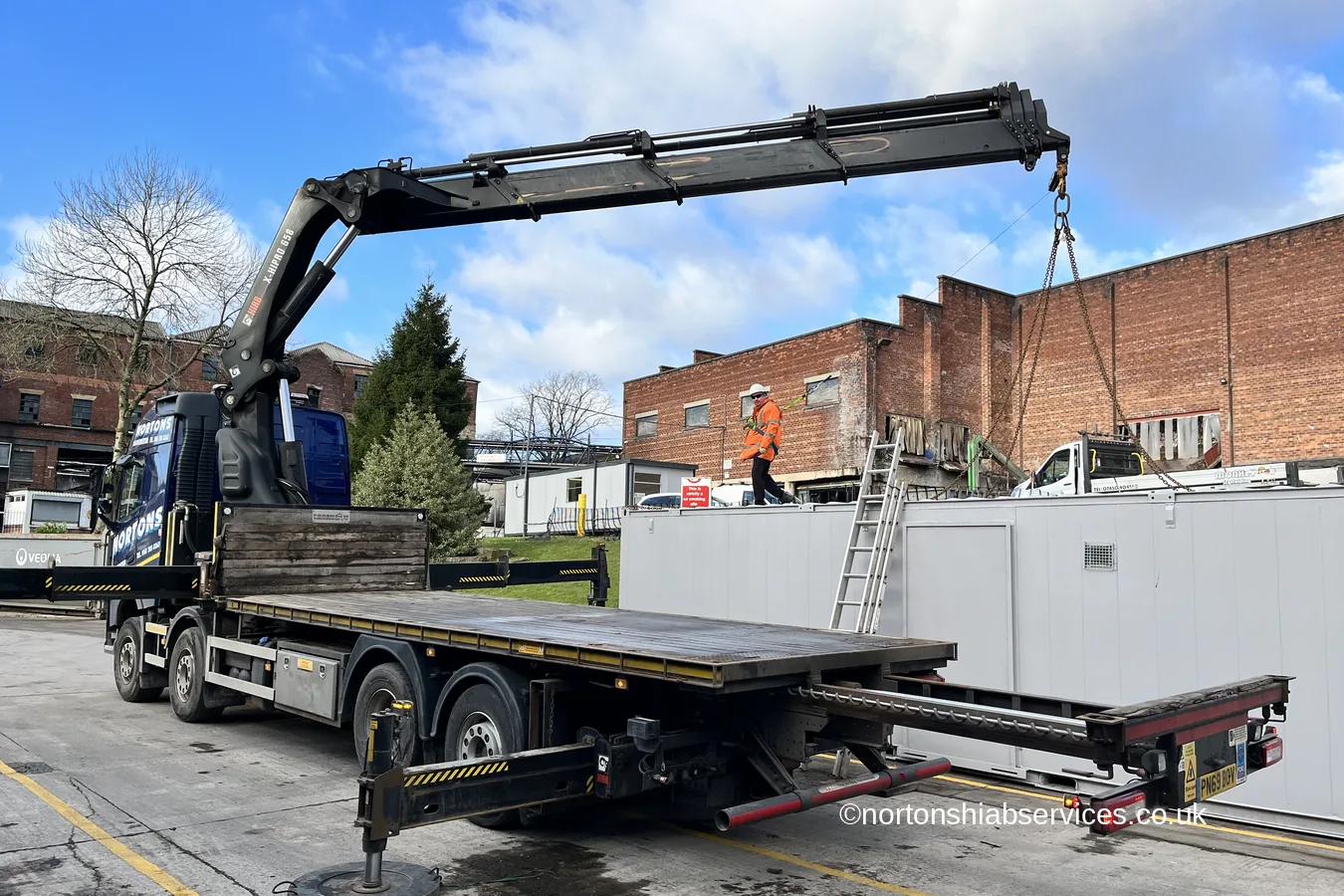 The empty bed of a Nortons crane lorry with the delivered cabins standing behind it at Romiley